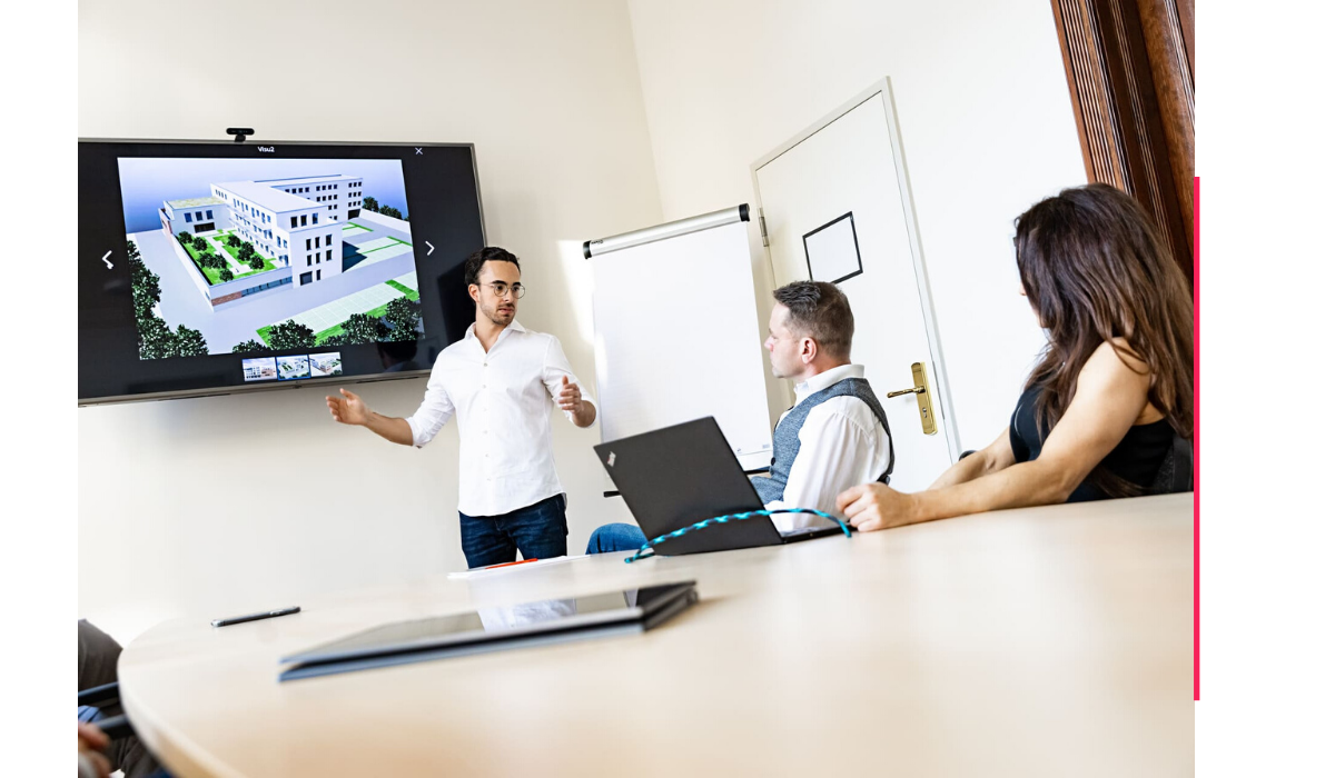 Maximilian Wöber von Wöber Immobilien präsentiert Kunden und seinen Mitarbeitern die Vertriebsstrategie zum Bauträgervertrieb in einem Meeting Raum.